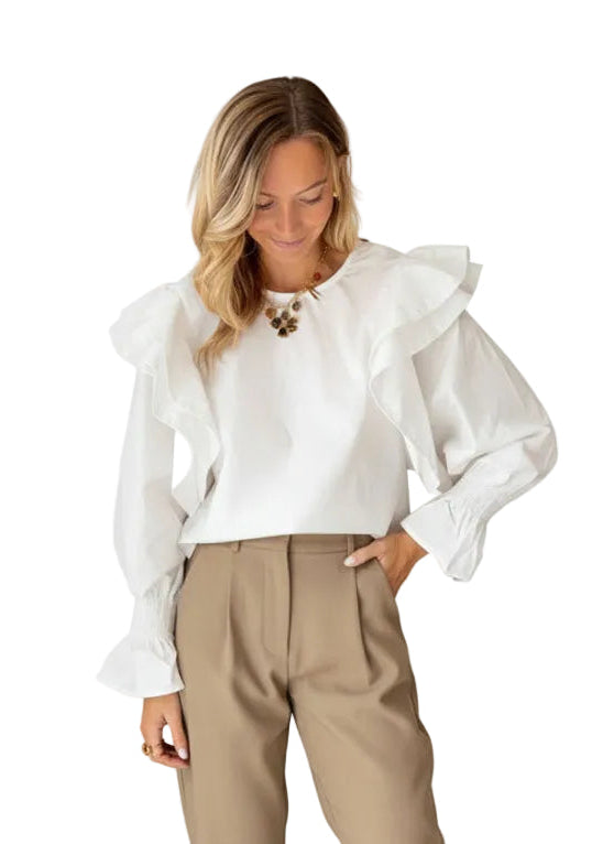 Woman wearing a white blouse with ruffled sleeves and beige pants on a white background