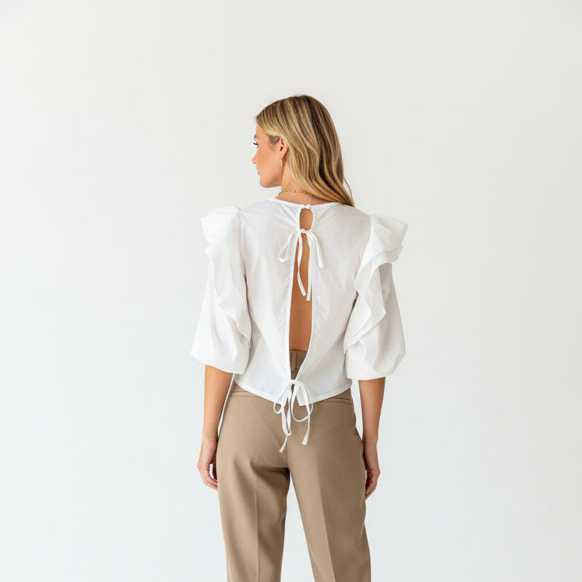 Woman wearing a white blouse with ruffled sleeves and tied back design against a wooden background