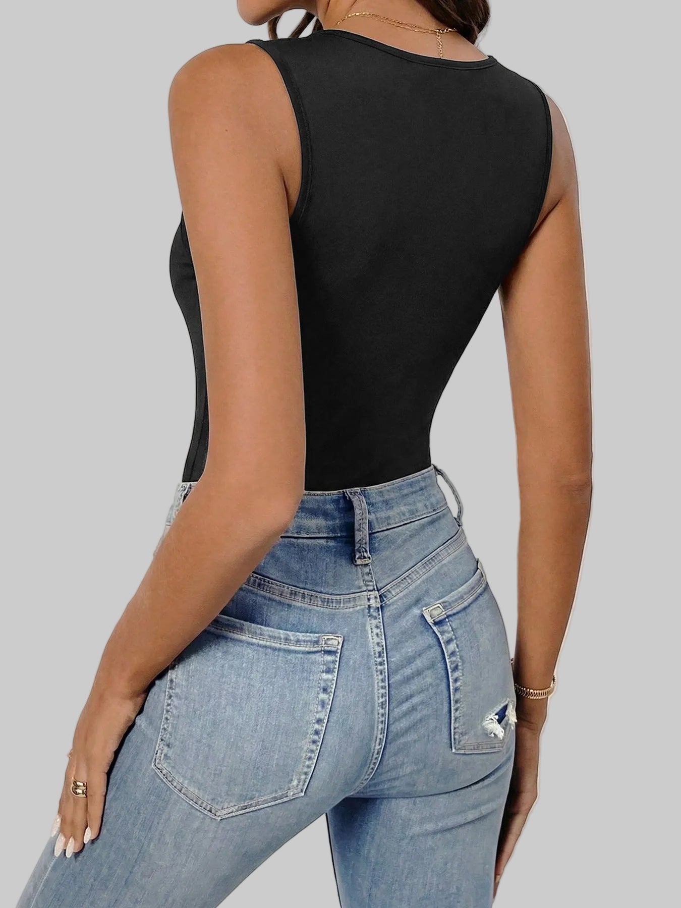 Person wearing a black sleeveless top and blue jeans with a white wall and blue door in the background.