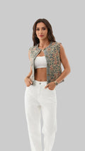 Woman wearing a floral denim vest over a white top and pants, standing outdoors.