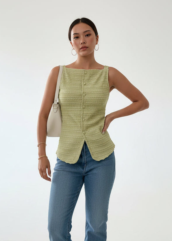 Person wearing a light green textured sleeveless top with blue jeans indoors.