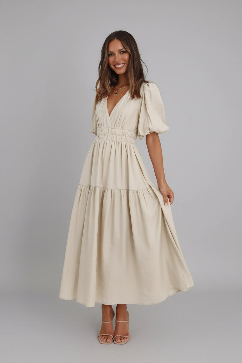 Woman wearing a beige dress with puff sleeves in a minimalistic room.
