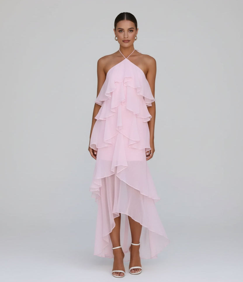 Woman wearing a pink ruffled dress standing against a stone wall.