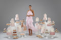 Woman wearing a pink ruffled dress standing around cakes